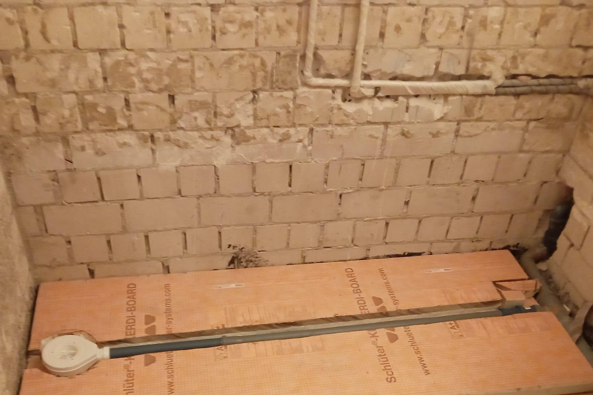 Unterkonstruktion aus Hartschaum-Verbundplatten auf Sockel mit verlegtem Rinnenrohr vor Bestandsziegelwand
